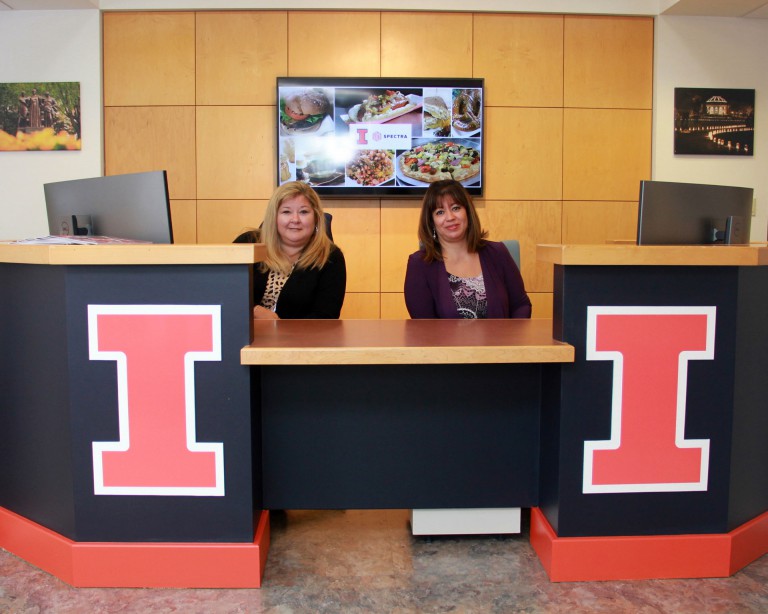 Two smiling employees at UIUC front desk