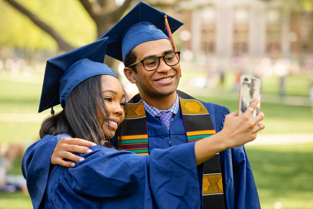 Two people in graduation gowns taking a selfie